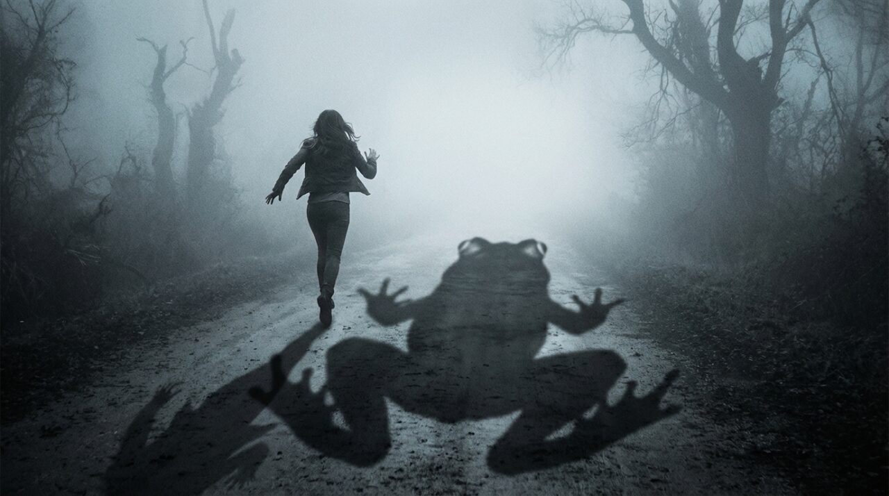 霧の中で何かに追いかけられ、焦って走る女性の後ろ姿。足元には巨大なカエルの影が伸びている